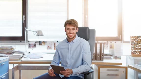 En mann sitter på en kontorstol med et nettbrett i hånden.