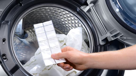 Hand holding a ProHygiene test in front of the drum of a professional Miele washing machine containing white laundry.