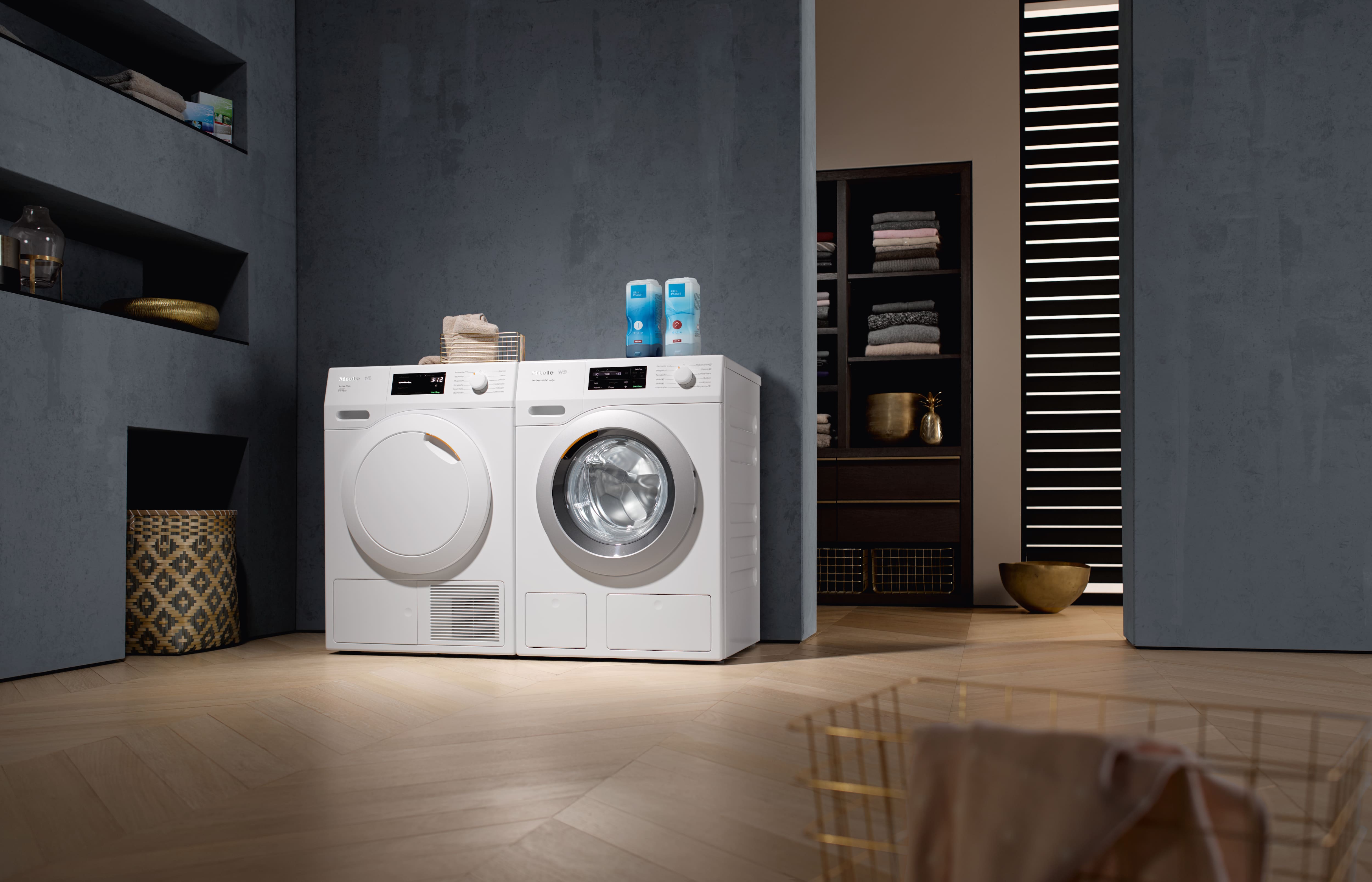 Pyykinpesukone ja kuivausrumpu vierekkäin, TwinDos‑säiliöt päällä, kodinhoitohuoneympäristössä.