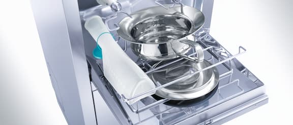Detailní záběr na otevřený mycí a dezinfekční automat podložních mís naplněný močovými lahvemi a podložními mísami.