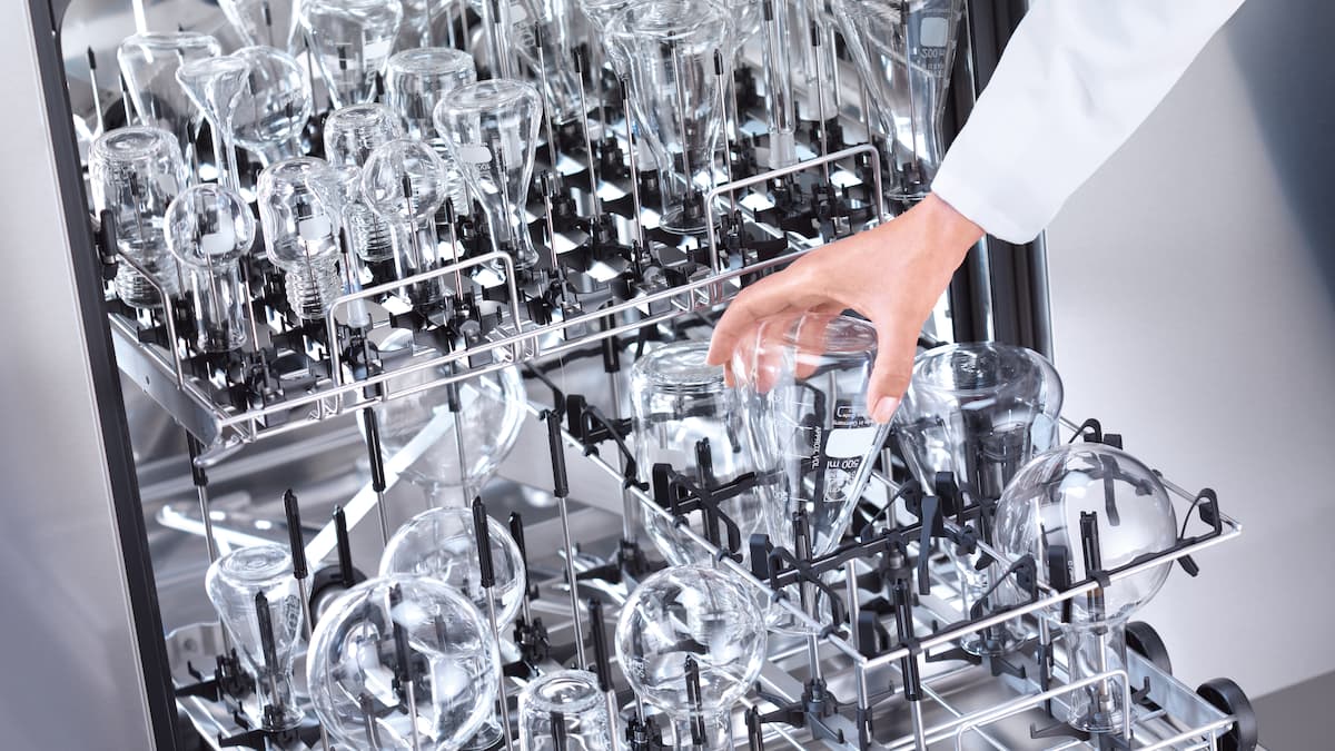 Hand removes clean, shining crockery from a dishwasher.