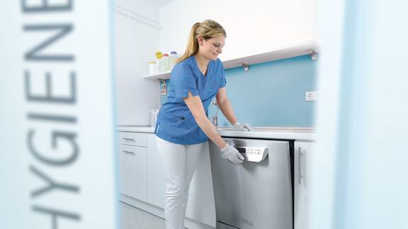 Une assistante médicale ouvre un laveur-désinfecteur dans la salle de traitement.