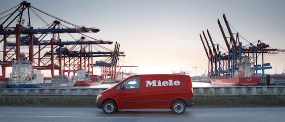 Red Miele Service car drives on a bridge at a port.