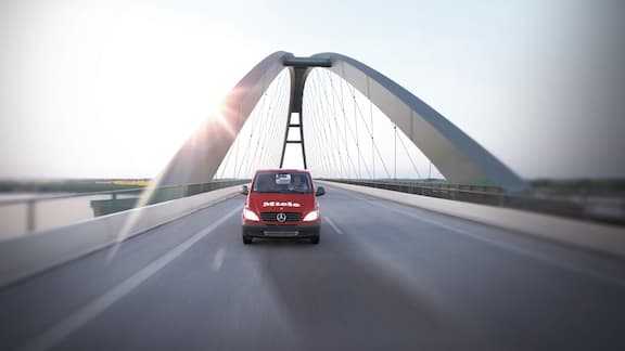 Red car driving on bridge with the sun in the background.