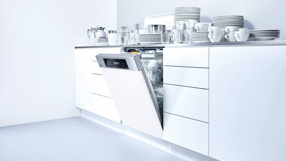 Bancada de cozinha branca com máquina de lavar louça branca encastrada, onde há pratos na bancada.