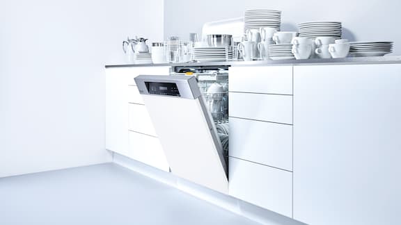 Weisse Küchenzeile mit eingebautem weissem Geschirrspüler, wo auf der Arbeitsplatte Geschirr steht.
