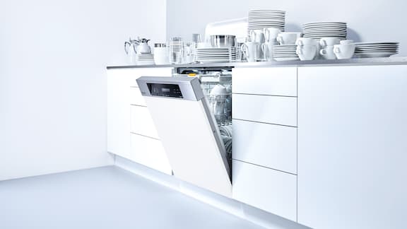 White kitchenette with integrated white dishwasher and crockery on the work surface.