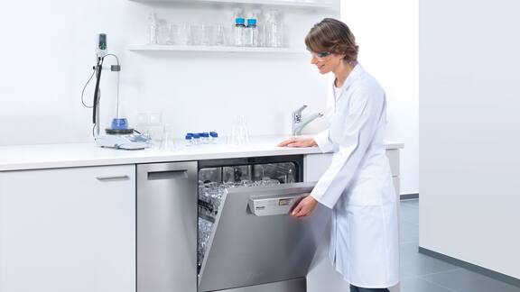 En kvinnelig ansatt ved et laboratorium lukker en full laboratoriemaskin for plassering under benk.