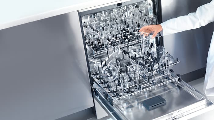 Opened laboratory glasswasher with different kinds of laboratory glassware placed in the baskets.