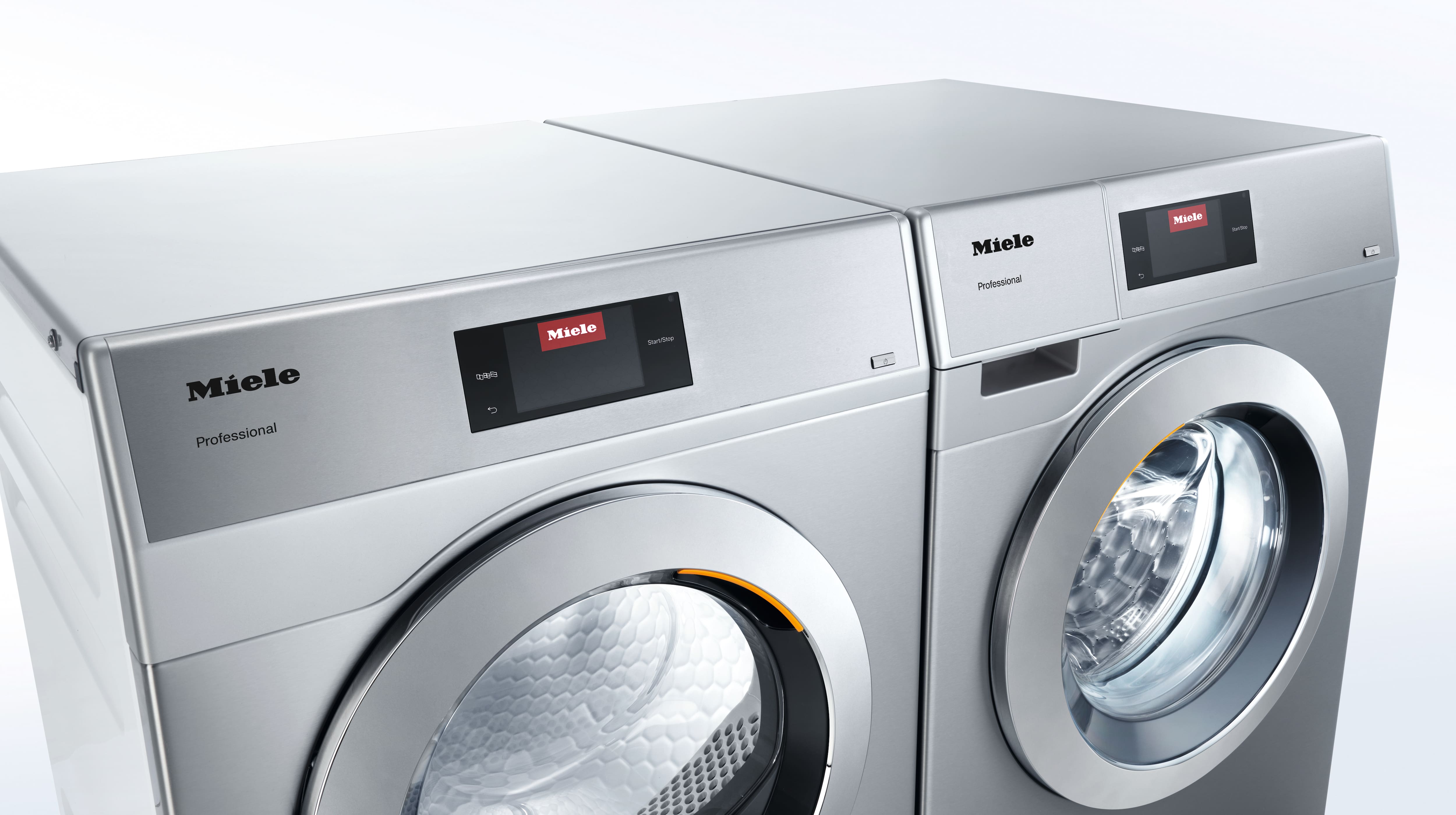 A room contains commercial washing machines from the Miele Professional SmartBiz, Little Giants and Benchmark series. Towels have been left on Little Giants and Benchmark washing machines. The door of the Little Giants washing machine is half open and a towel is sticking out.