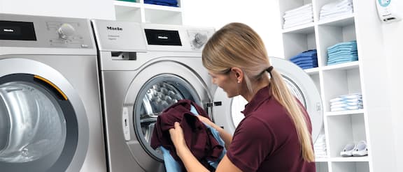 Assistente dentária coloca roupa na máquina de lavar roupa.
