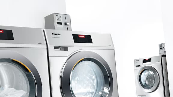 Stainless steel commercial washing machines in minimalist surroundings.