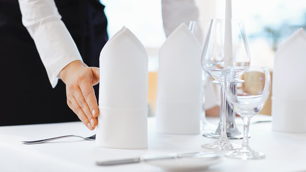 Des mains disposent des serviettes blanches sur une table.