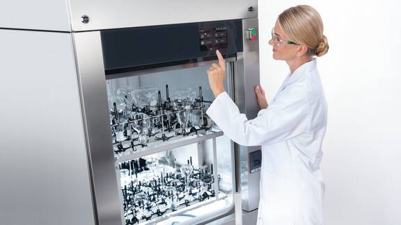 Laboratorioteknikko käyttämässä täytettyä suurta laboratoriopesukonetta.