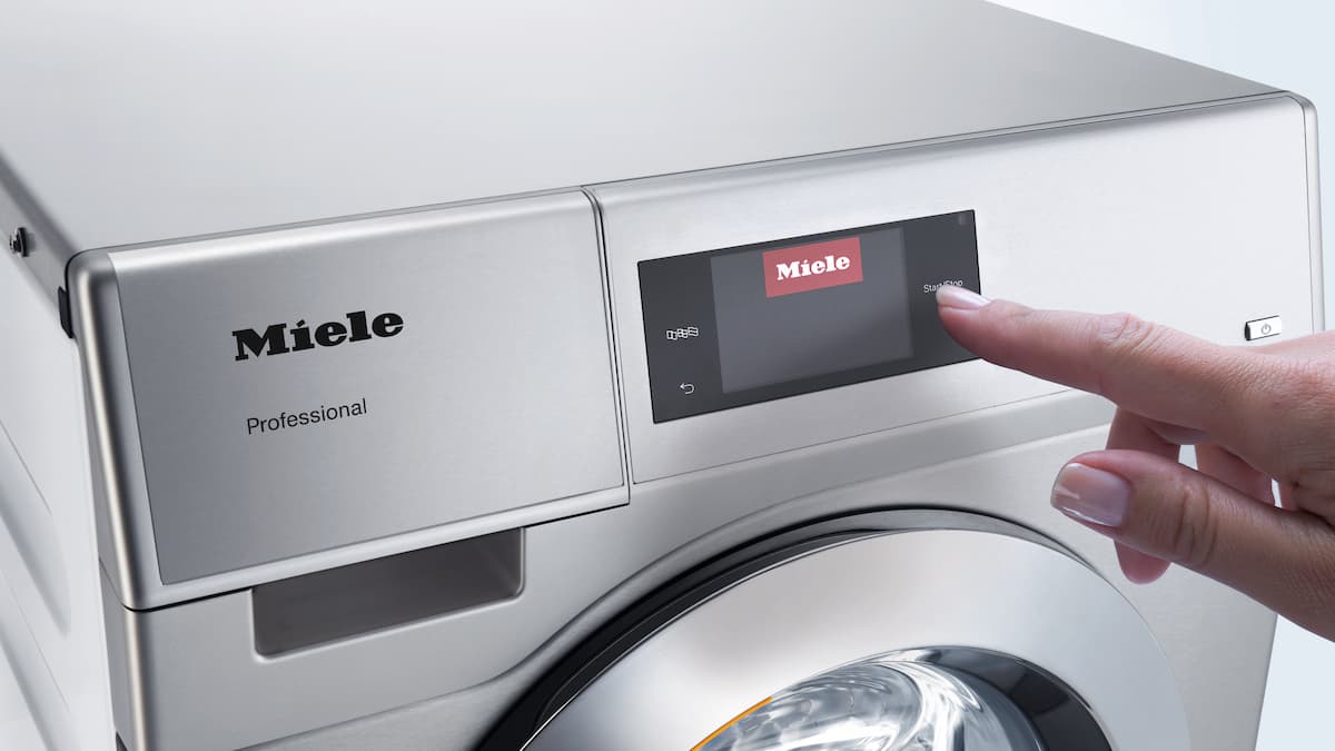Hand operates the display of a commercial Miele Professional washing machine.