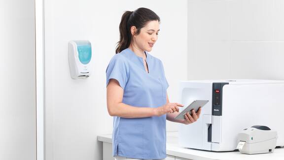 L’assistante médicale tape sur une tablette, debout devant un stérilisateur compact.