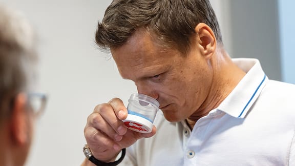 Ein Mitarbeiter der Firma Symrise riecht an einer Duftprobe mit dem Symrise Logo.