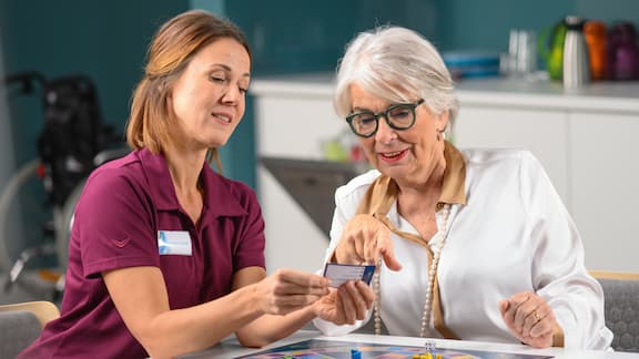 Verpleegkundige legt bordspel uit in een verpleeghuis.