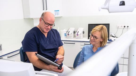 Un odontoiatra mostra qualcosa su un tablet  a una paziente