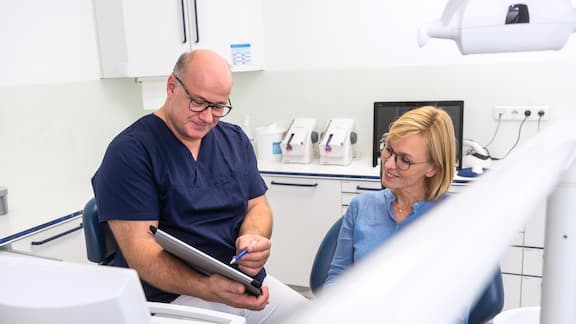 A male dentist shows a female patient something on a tablet