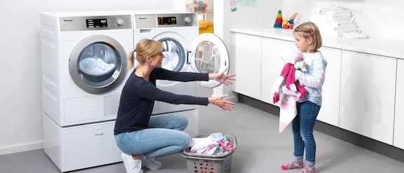 Een kind geeft wasgoed aan een vrouw in de wasruimte.