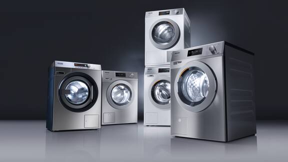 Fünf graue Waschmaschinen und Trockner angeordent vor einem dunklem Hintergrund.