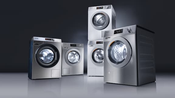 Vijf grijze wasmachines en droogkasten gerangschikt tegen een donkere achtergrond.