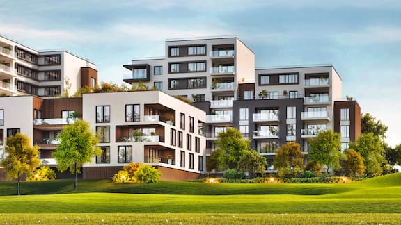 Complexe d’appartements moderne devant une pelouse verdoyante et sous un ciel bleu.