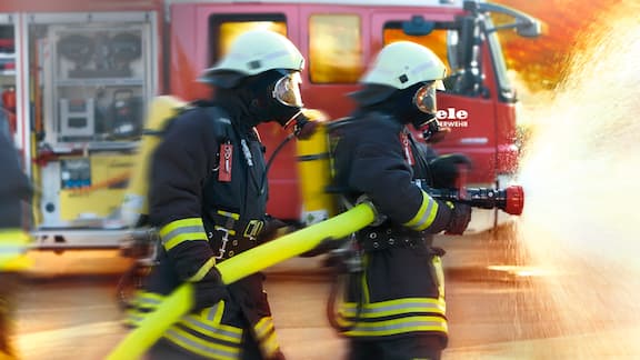 To brannmenn i fullt utstyr slukker en brann.