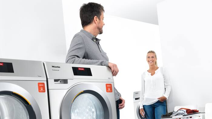 Δύο ενήλικα άτομα συζητούν σε μια αίθουσα πλυντηρίων που λειτουργούν μέσω της εφαρμογής appWash.