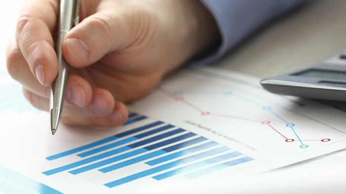 Hand with pen checks printed bar chart and calculator lies next to it