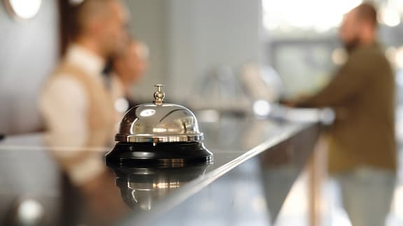 Primo piano del campanello alla reception di un albergo. Receptionist e ospite sullo sfondo