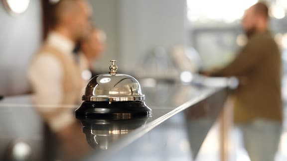 Close-up of handbell in hotel reception. Receptionist and guest in the background