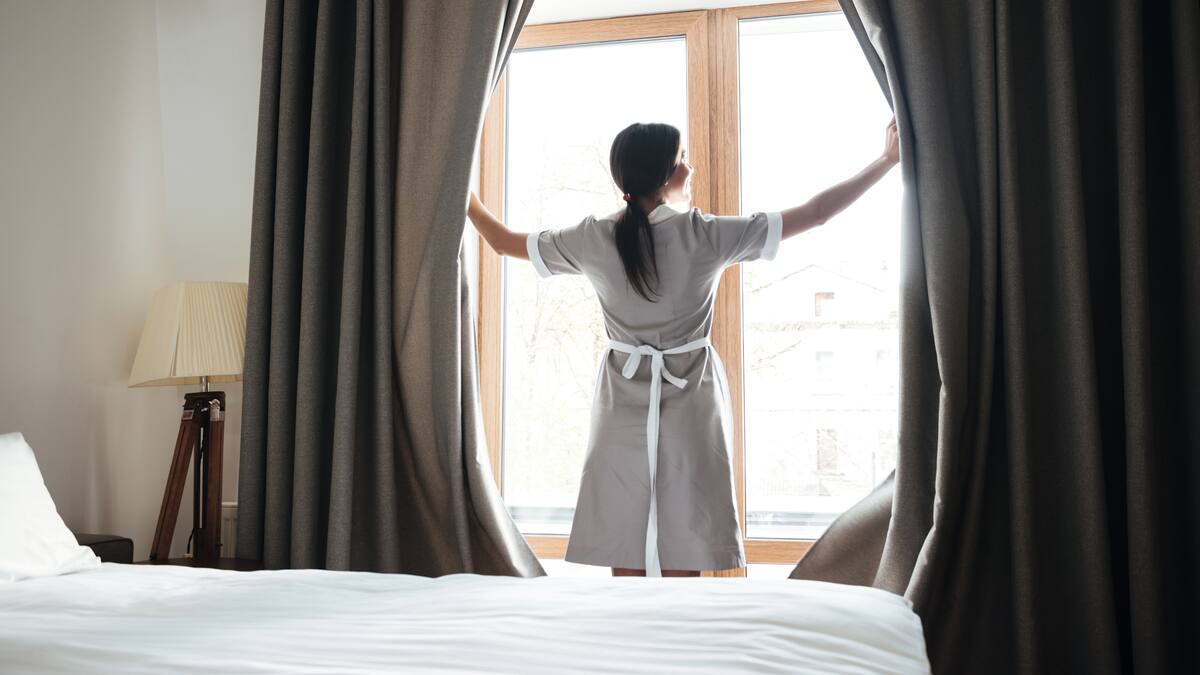 Une femme de chambre qui ouvre les rideaux d'une chambre d'hôtel