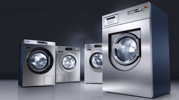 Four grey washing machines and dryers in front of a dark background.