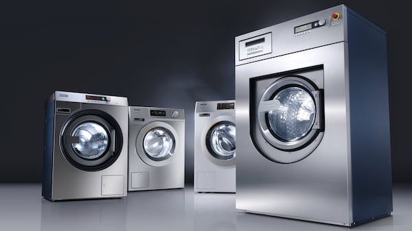 Vier graue Waschmaschinen und Trockner vor dunklem Hintergrund.