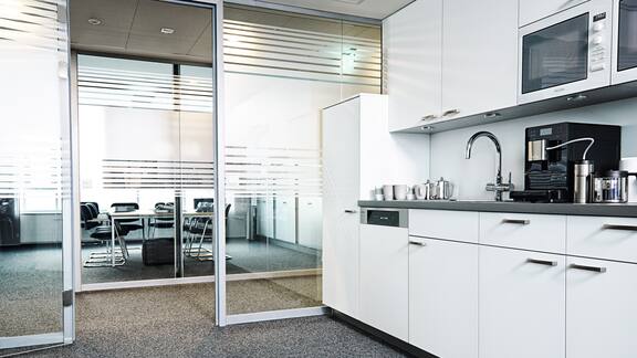 White staff kitchen in an office with glass doors.