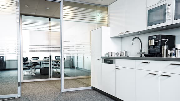 Cocina de trabajo blanca en la oficina con puertas de cristal.