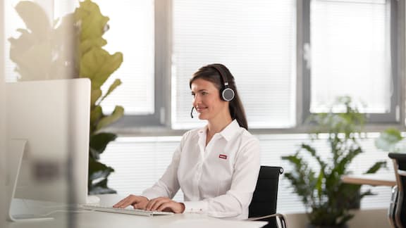 Γυναίκα που φορά σετ μικροφώνου-ακουστικών κάθεται σε γραφείο σε τηλεφωνικό κέντρο.