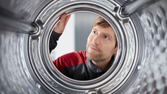 Miele Professionals servicetekniker tittar in genom skontrumman på en professonell tvättmaskin