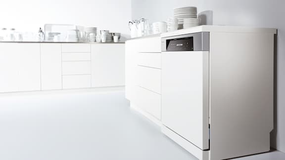 Weiße Küchenzeile mit eingebautem weißem Geschirrspüler, wo auf der Arbeitsplatte Geschirr steht.