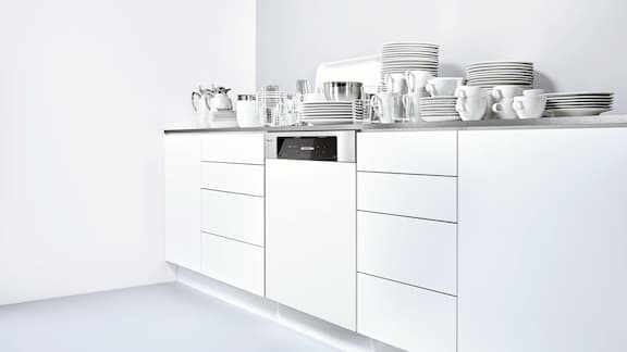 Una cucina bianca con lavastoviglie bianca da incasso e molte stoviglie sul piano di lavoro.