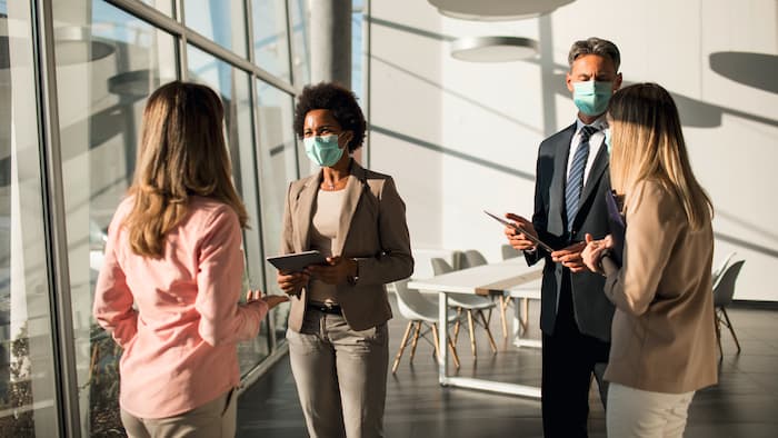 Work colleagues wearing masks have a discussion in a meeting room.