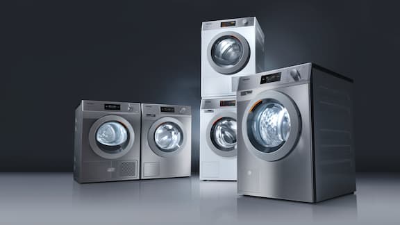 Five grey washing machines and dryers arranged in front of a dark background.