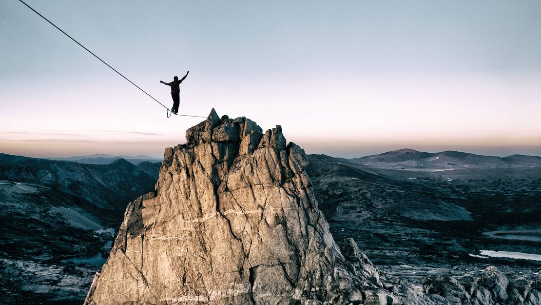 Un adepte de slackline en équilibre sur un câble menant au sommet d’une montagne 