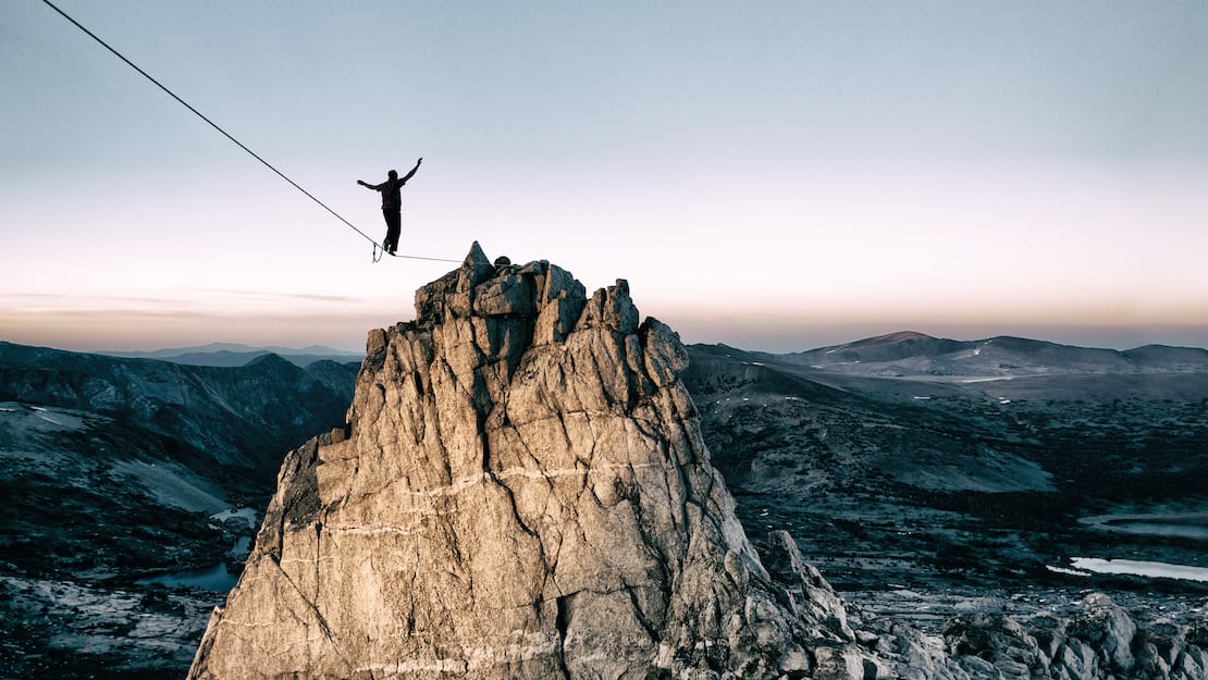 Slackliner is balancing on a rope facing the mountain summit 