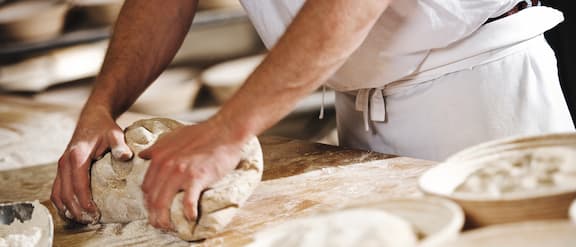 Baker kneads dough on a wooden work surface.