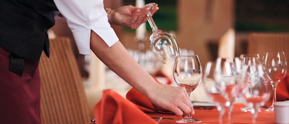 Mani che al ristorante apparecchiano la tavola con calici da vino.