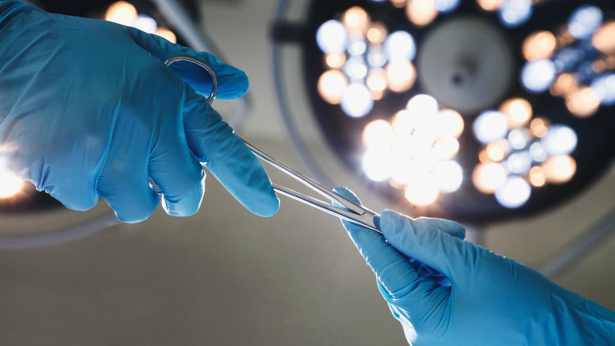 Hands in surgical gloves hold instruments.