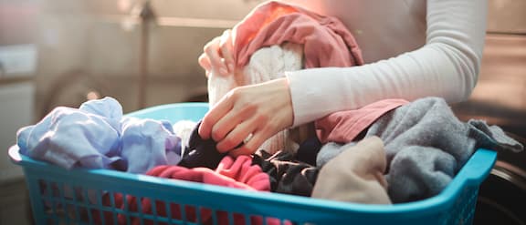 Unas manos clasifican ropa de color con lavadoras Miele de fondo.